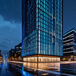 A futuristic cityscape at twilight, dominated by a magnificent skyscraper featuring an advanced, AI-generated interactive media facade. The building's exterior glows with dynamic, abstract patterns and vibrant light, reflecting on the wet pavement below. Surrounding buildings are subtly lit, creating a sense of depth and urban energy. The scene is illuminated by intelligent lighting, highlighting modern architectural details. This is a professional architectural photograph, capturing the essence of a smart city at night. safe for work, appropriate content, fully clothed, professional, perfect anatomy, correct proportions, natural body proportions, high quality.